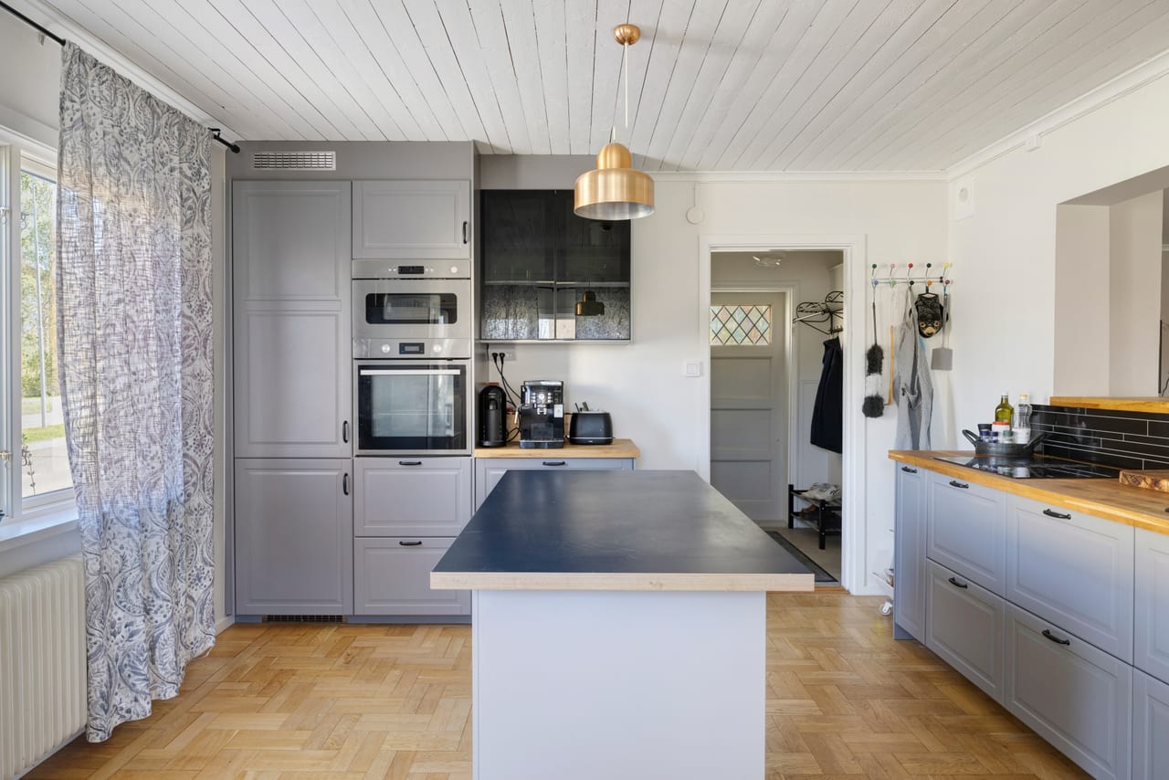 Kök med grå skåp, köksö och fiskbensparkett.