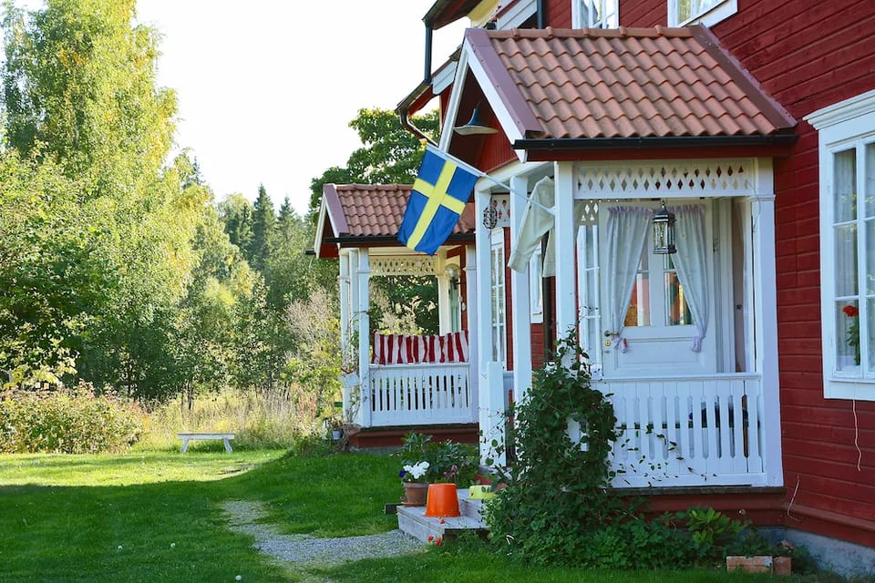 Rött trähus med vit veranda och svensk flagga.