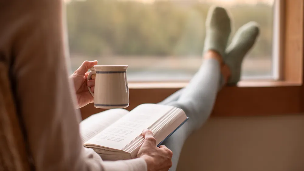 Person som vilar med en kopp kaffe och en bok i ett ljust rum